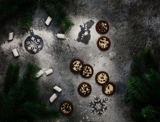 assorted cookies and marshmallows on dark blue background with snowman and snowflake prints made of sugar powder among pine branches, top view