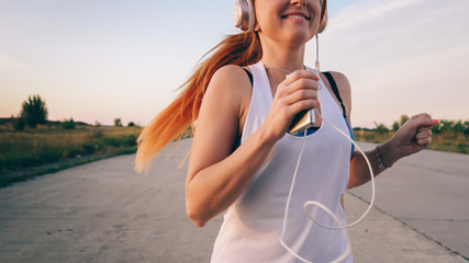young woman runs and listens to music on headphones on a summer afternoon at sunset, close-up - obrazy, fototapety, plakaty