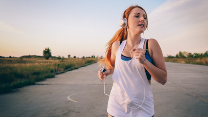young woman runs and listens to music on headphones on a summer afternoon at sunset