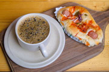 Cup of coffee and mini pizza on wooden cutting board