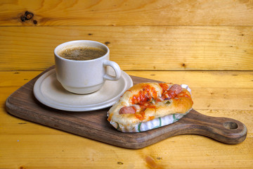 Cup of coffee and mini pizza on wooden cutting board