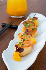 Delicious pan seared organic scallops, served with orange segments on a white plate. Presented professionally and shot with a shallow depth of field.