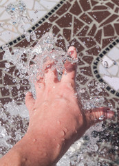 A caucasian hand reaching into a spurting water fountain causing splashes and water droplets to form. Very refreshing and wet, cooling down on a hot day.