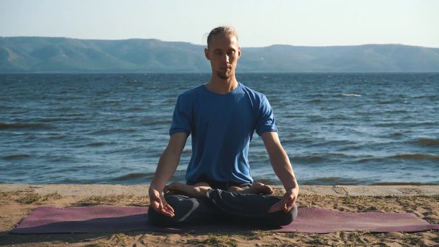 young man in meditation near the ocean, mountains on background