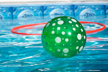 green and white spotted beach ball floating in a swimming pool