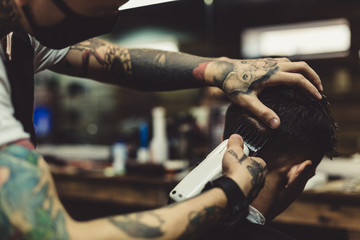 Crop tattooed stylist concentrated on shaving man with machine doing hairstyle.