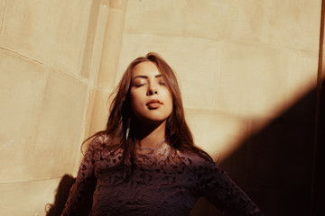 Sensual brunette model with closed eyes posing at the courtyard with shadow on her face