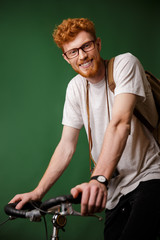 Young cheerful readhead bearded hipster with backpack and retro camera, ready to ride bicycle