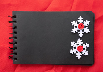 Simple New Year handmade frame. Black notebook , snowflakes on red fabric. Space for text, place for message.