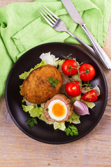 Scotch eggs on a plate with cherry tomatoes and salad. View from above, top studio shot, vertical