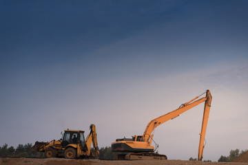 tractor and excavator on a large sand pile under the blue sky