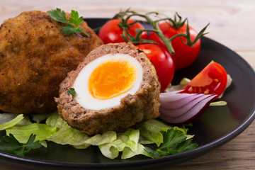 Scotch eggs on a plate with cherry tomatoes and salad, horizontal