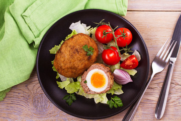 Scotch eggs on a plate with cherry tomatoes and salad. View from above, top studio shot, horizontal