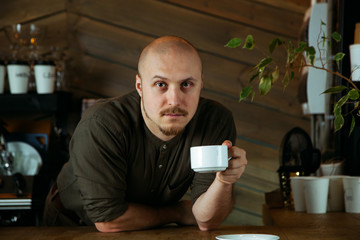 Young friendly bartender with mustache and beard standing at the bar counter in loft-styled cafe. Former factory building, natural daylight.