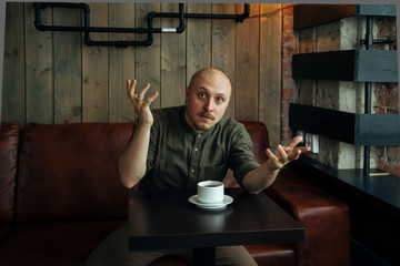 Young serious fashionable man having conflict discussion in loft-styled cafe. Former factory building, natural daylight.