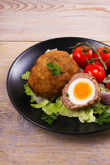 Scotch eggs on a plate with cherry tomatoes and salad, vertical