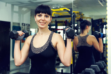 Fototapeta na wymiar An adult woman holding dumbbell lifting up. Client fitness center. Young woman doing workout with weights on the fitness gym background. Woman working out with dumbbells in gym. Sport modern woman.