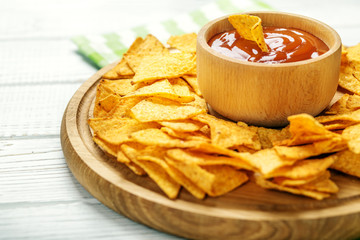 Delicious Mexican Nachos Chips on a Wooden Tray. Spicy sauce wit