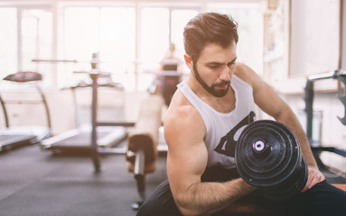 Fototapeta na wymiar Muscular Bearded man during workout in the gym. Athlete muscular bodybuilder in the gym training biceps with dumbbell. Indoor fitness