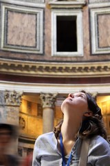 Young woman tourist looking above and admiring the beauty of Pantheon in Rome, Italy. On excursion with audio guide and headphones