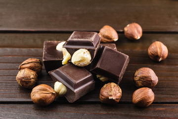 Pieces of bitter dark chocolate cubes with hazelnut on heap at wooden background, close-up view