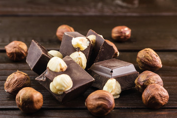 Pieces of bitter dark chocolate cubes with hazelnut on heap at wooden background, close-up view