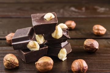 Pieces of bitter dark chocolate cubes with hazelnut on heap at wooden background, close-up view