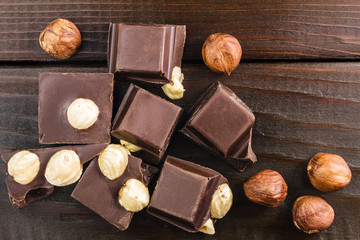 Pieces of bitter dark chocolate cubes with hazelnut on wooden planks background, top view