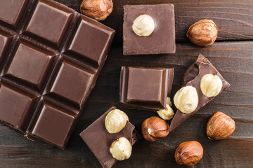 Pieces of bitter dark chocolate cubes with hazelnut on wooden planks background, top view