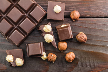 Pieces of bitter dark chocolate cubes with hazelnut on wooden planks background, top view