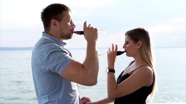 A man and a woman who flirt with each other clink glasses with wine, the couple celebrate the anniversary of marriage in a restaurant with an open terrace