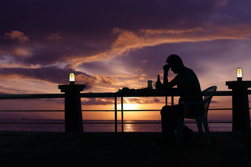 Silhouette sad man drinking beer at the beach with red sky sunset