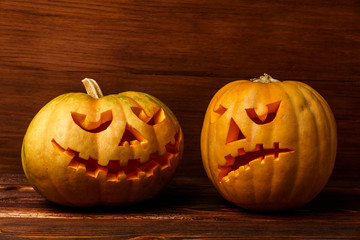 Scary Halloween pumpkins isolated on wooden background . Scary glowing faces trick or treat. Concept of halloween pumpkin on wooden planks. Two halloween pumpkins on wooden background