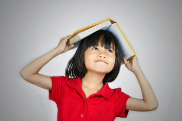 young asian girl holding book on head isolated on white background .