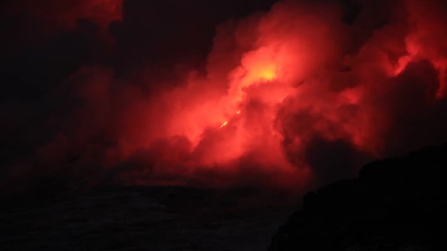 Night shot of lava flowing into the ocean with red fire and steam clouds