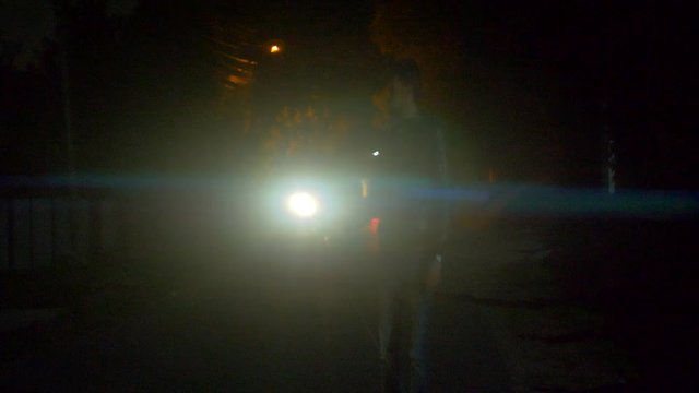 The man with a flashlight walking on the road. night time. anamorphic lens shot