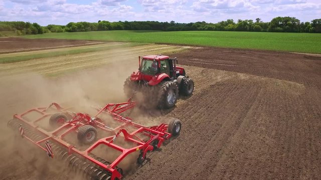 Agricultural tractor with trailer plowing on farming field. Sky view farming tractor driving on plowing field. Agricultural industry. Farming machinery. Agricultural sector. Tractor ploughing