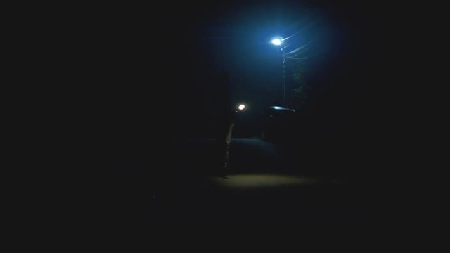 The man walking with a flashlight on the street. night time. anamorphic shot