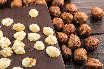Part of bitter dark chocolate bar with hazelnut on wooden planks background, close-up view