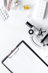 Doctor's workplace. Microscope, tablet, pills and test tube on white background top view copyspace mockup