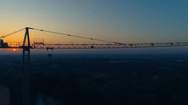 Aerial Shot of the Industrial Crane with Dark Cityscape and Setting Sun in the Background. Shot on a Camera in 4K (UHD).