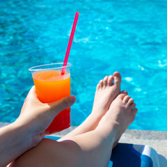 summer, travel and vacation concept - female hand holding cocktail over swimming pool background