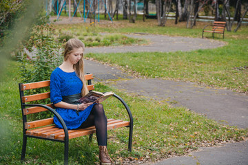 The girl reads the book in the park. The girl in the park sits on a shop. Walk on the park in the summer.