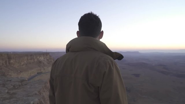 Man looking at the desert view from the edge of a cliff