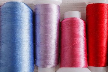 Colorful thread spools on wooden table close up