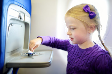 Adorable little girl traveling by an airplane. Child sitting by aircraft window and playing with toy plane. Traveling with kids.