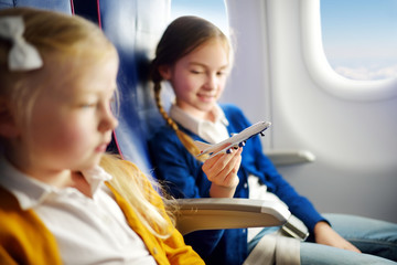 Adorable little girls traveling by an airplane. Children sitting by aircraft window and playing with toy plane. Traveling with kids.