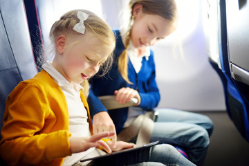Adorable little girls traveling by an airplane. Children sitting by aircraft window and using a digital tablet during the flight. Traveling with kids.