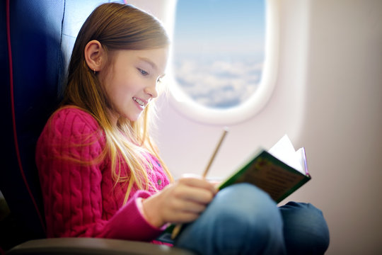 Adorable little girl traveling by an airplane. Child sitting by aircraft window and drawing a picture with colorful pencils. Traveling with kids.