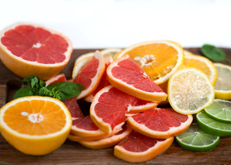 sliced citrus decorated with basil on wooden and white backgrounds. Orange, grapefruit, lime, lemon.